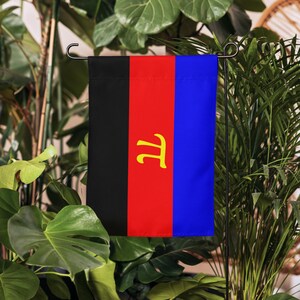 May include: A vertical garden flag with a design featuring three vertical stripes in black, red, and blue. A yellow symbol is centered on the red stripe. The flag is displayed on a black metal stand, surrounded by green plants.