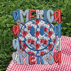 May include: Embroidered design featuring the word "AMERICA" in red, white, and blue, with a smiley face at the center. The smiley face is filled with a floral pattern in red, white, and blue. The design is on a red and white checkered background.