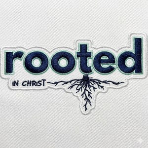 May include: Embroidered patch with the word "rooted" in navy blue letters with a light green outline. Below the word is the phrase "in Christ" and a graphic of roots. The patch is on a white background.