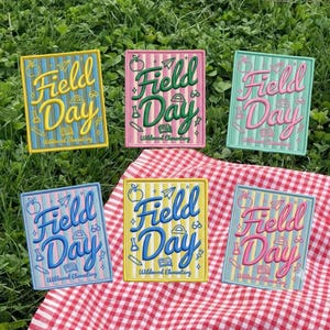 May include: Six embroidered patches with the words "Field Day" in various colors, including yellow, pink, blue, and green. Each patch has a rectangular shape with a yellow border and includes the text "Wildwood Elementary".