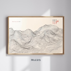 May include: A framed print featuring a black and white line drawing of a mountain range. The artwork includes the text "Mon Fuji, Japan 1903" and Japanese characters. The frame is a light brown color, and the print is displayed on a white wall.
