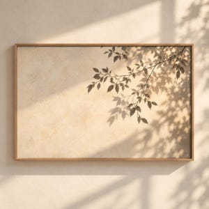 May include: A rectangular wall art piece featuring a light beige, textured background with a dark brown shadow of a leafy tree branch cast across the surface, all enclosed within a thin, light-colored wooden frame.