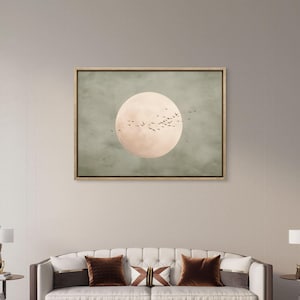 May include: A framed canvas art piece featuring a large, pale peach-colored circle, possibly representing the sun or moon, set against a muted green background. Silhouettes of birds fly across the circle. The artwork is displayed above a sofa.