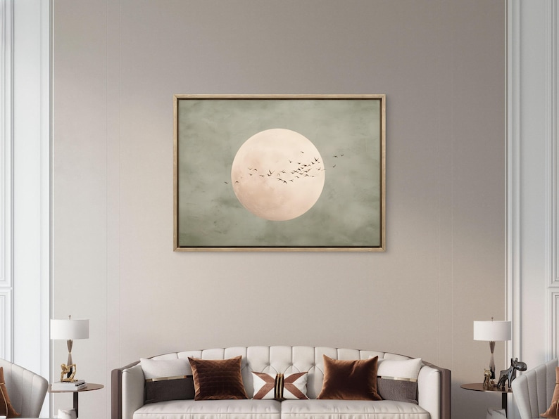 May include: A framed canvas art piece featuring a large, pale peach-colored circle, possibly representing the sun or moon, set against a muted green background. Silhouettes of birds fly across the circle. The artwork is displayed above a sofa.