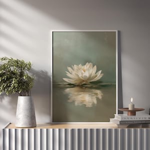 May include: A framed art print featuring a white lotus flower floating on water. The artwork has a soft, muted color palette with a reflective surface. A vase with greenery and a candle are on a nearby surface.
