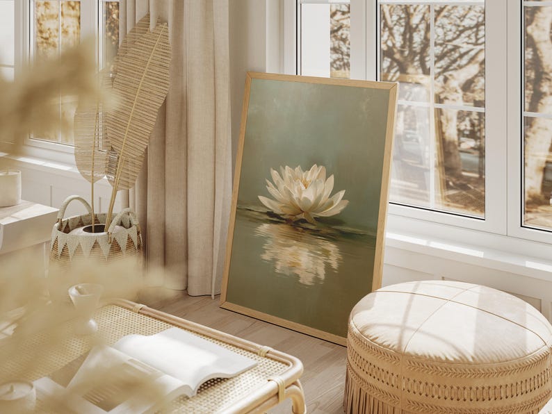 May include: A framed art print featuring a white water lily floating on water. The artwork has a soft, muted color palette with a light wooden frame. The scene is set in a bright, airy room with natural light.