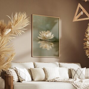 May include: A framed art print featuring a white lotus flower reflected in water. The artwork hangs above a beige sofa with decorative pillows and a patterned throw. Dried plants and wooden geometric light fixtures add to the room's decor.
