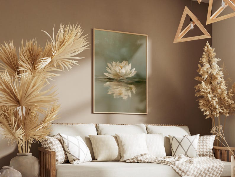 May include: A framed art print featuring a white lotus flower reflected in water. The artwork hangs above a beige sofa with decorative pillows and a patterned throw. Dried plants and wooden geometric light fixtures add to the room's decor.
