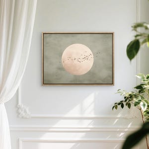 May include: A framed art print featuring a large, pale pink circle resembling a moon against a muted green background. Silhouetted birds fly across the moon. The artwork is displayed on a white wall.