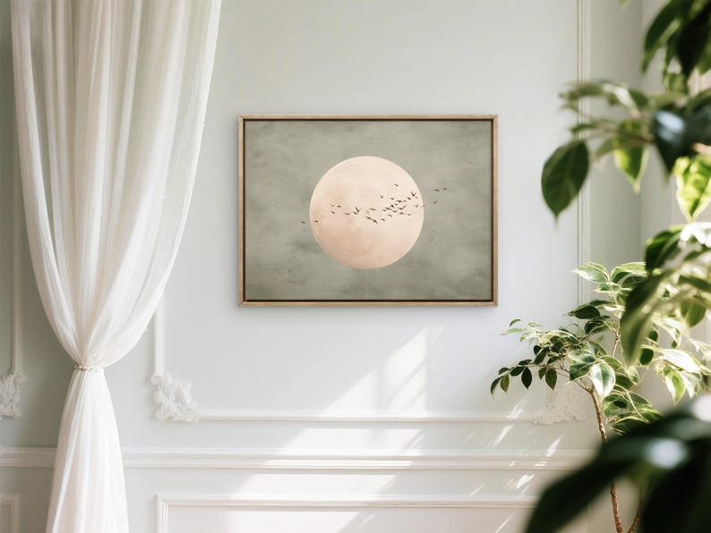 May include: A framed art print featuring a large, pale pink circle resembling a moon against a muted green background. Silhouetted birds fly across the moon. The artwork is displayed on a white wall.