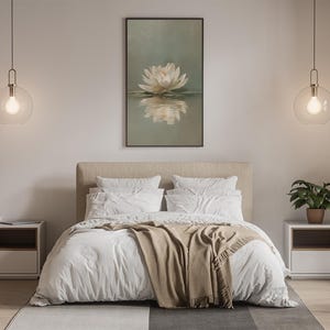May include: Bedroom interior with a large bed, white bedding, and a tan throw blanket. A framed artwork of a white flower is above the bed. Two pendant lights with round glass shades hang on either side of the bed. A small potted plant sits on a nightstand.