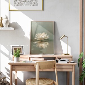May include: A light wood desk with a framed lotus flower print, a small potted plant, and a gold desk lamp. A wooden chair is positioned in front of the desk. The room has a neutral color palette with natural light.