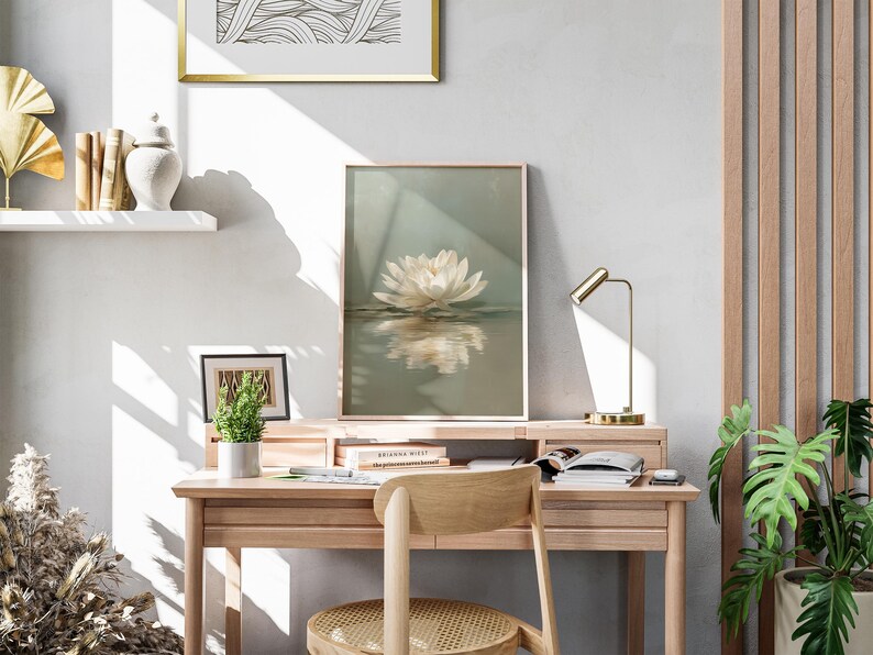 May include: A light wood desk with a framed lotus flower print, a small potted plant, and a gold desk lamp. A wooden chair is positioned in front of the desk. The room has a neutral color palette with natural light.