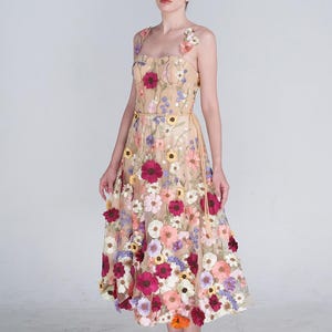 May include: A midi-length dress in a nude, sheer fabric featuring a sweetheart neckline and thick straps. The dress is adorned with a dense, multi-colored floral appliqué pattern in shades of red, pink, yellow, purple, and white throughout.