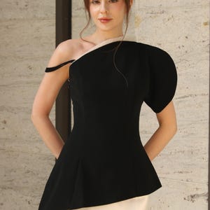 Peut inclure: Un haut noir à une épaule avec une bordure blanche et un design péplum. Il est associé à une jupe blanche. L'ensemble est élégant, adapté aux événements formels ou aux occasions spéciales.