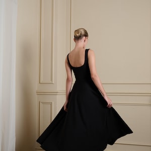 May include: A solid black midi dress featuring a wide scoop neckline, thick shoulder straps, and a flared skirt that falls below the knees. The garment is paired with black pointed-toe high-heeled pumps, creating a cohesive and structured appearance.