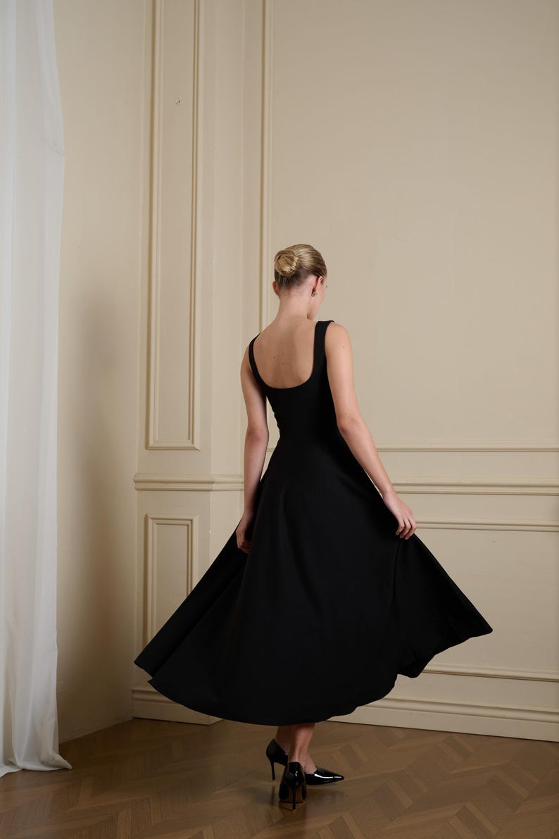 May include: A solid black midi dress featuring a wide scoop neckline, thick shoulder straps, and a flared skirt that falls below the knees. The garment is paired with black pointed-toe high-heeled pumps, creating a cohesive and structured appearance.