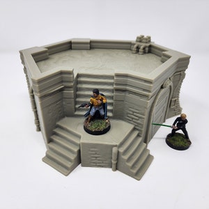 May include: A gray, octagonal, 3D printed building with a flat roof and a doorway. The building has two sets of stairs leading up to the roof. Two miniature figures are standing on the roof and stairs.
