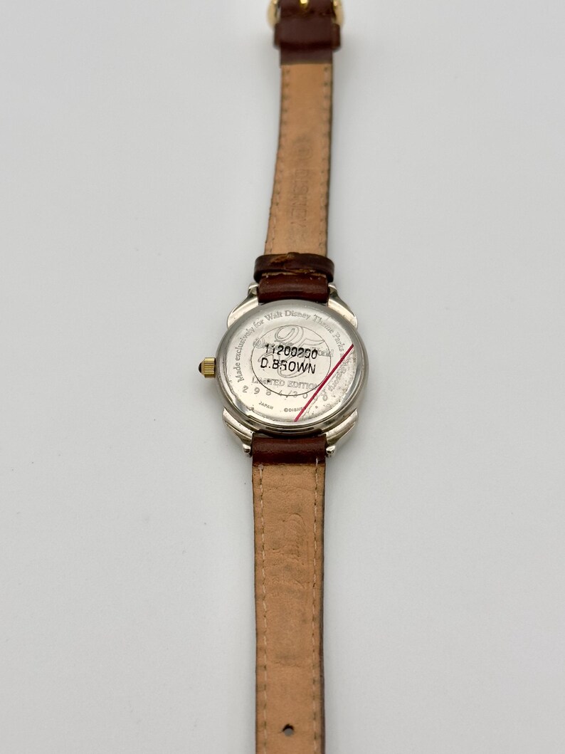 May include: A silver-toned wristwatch with a brown leather band. The watch face is white with black text and a red line. The band is 0.5 inches wide. The watch is a limited edition.