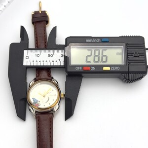 May include: A vintage wristwatch with a brown leather band and a gold-toned bezel. The watch face features a Mickey Mouse design. The digital caliper shows the watch is 28.6 mm wide. The watch is being measured against a white background.