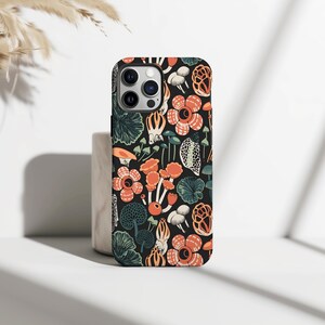 May include: Black phone case featuring a botanical pattern of orange flowers, green leaves, and mushrooms. The design is set against a dark background. The case is shown on a white surface.