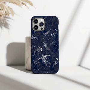 May include: A navy blue phone case featuring a white illustration of various sea creatures, including sharks, whales, and jellyfish, set against a starry background. The case has a glossy finish and a protective bumper.