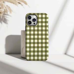 Può includere: Una custodia per telefono con un motivo a quadretti verde e bianco sporco. La custodia ha un bordo nero e un ritaglio per la fotocamera. La custodia è su una superficie bianca.