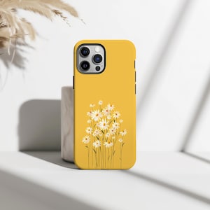 May include: A yellow phone case with a design of white daisies with yellow centres and green stems. The case has a glossy finish and a black camera module. The design is a floral theme.