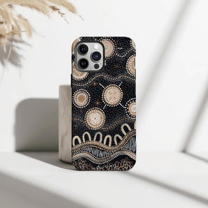 May include: A black phone case featuring a beige and white Aboriginal art design. The case has a repeating pattern of circles, dots, and curved lines. The phone case has a camera and flash cutout.