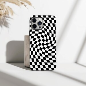 Puede incluir: Una funda de teléfono a cuadros blancos y negros. La funda tiene un patrón ondulado de cuadrados blancos y negros. La funda del teléfono está sobre una superficie blanca con un fondo neutro.