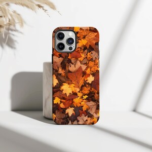 May include: A phone case featuring a vibrant autumn leaf design. The case showcases a collage of fallen leaves in shades of brown, orange, and yellow, creating a seasonal aesthetic. The case is designed to fit a smartphone.