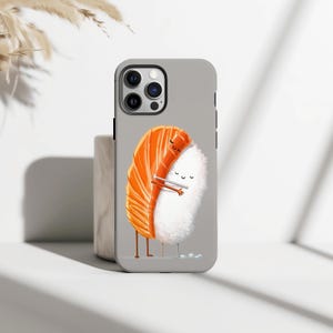 Puede incluir: Funda de teléfono gris con una ilustración de sushi de dibujos animados. El diseño muestra un nigiri de salmón abrazando una bola de arroz, con palillos chinos entre ellos. La funda tiene un módulo de cámara negro.