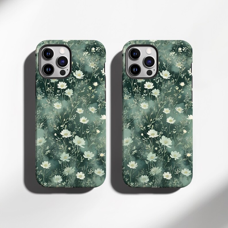 Op de afbeelding: Twee telefoonhoesjes met een bloemenpatroon. De hoesjes zijn donkergroen met een patroon van witte bloemen en groene bladeren. De hoesjes hebben een matte afwerking en zijn ontworpen voor een smartphone.