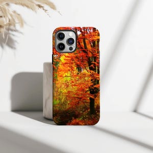 May include: A phone case featuring a vibrant autumn forest scene. The design showcases trees with fiery orange and red leaves, set against a backdrop of yellow and green foliage. The case is designed to fit a smartphone.