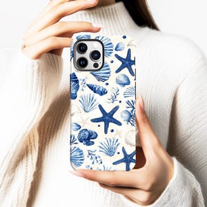 Pode incluir: Capa de telemóvel com um padrão repetitivo de estrelas do mar, conchas e corais azuis sobre um fundo creme. O design utiliza diferentes tons de azul, criando um tema náutico. A capa tem um acabamento brilhante.