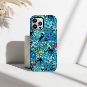 May include: A teal phone case featuring an underwater scene with black cats in space helmets, sea turtles, stingrays, and various fish. The design includes coral and seaweed elements, creating a whimsical, marine-themed pattern. The case has a glossy finish.