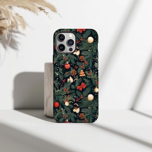 Può includere: Una custodia per telefono con un design a tema albero di Natale. La custodia è decorata con ornamenti, fiocchi rossi, pigne e bacche di agrifoglio su uno sfondo verde scuro. La custodia ha un bordo nero e un ritaglio per la fotocamera.
