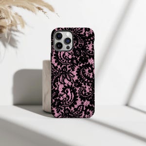 May include: A black and pink phone case with a lace pattern. The case has a glossy finish and a raised edge for screen protection. The detailed lace design includes floral and geometric shapes.