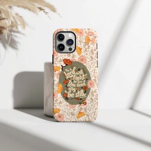 May include: A phone case with a floral design in peach, orange, and cream. The case has a quote in a green oval that reads, "The Lord will fight for you. You need only be still." The case has a glossy finish.