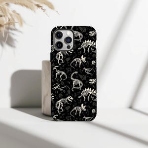 May include: Black phone case featuring a repeating pattern of white dinosaur skeletons. The design includes various dinosaur species and fossil elements. The case has a glossy finish and is designed to fit a smartphone.