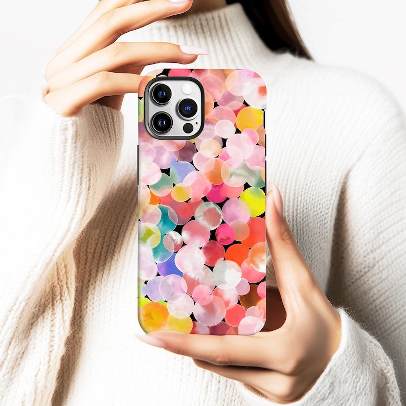 May include: A colorful phone case featuring a pattern of overlapping watercolor circles in shades of pink, orange, yellow, and blue against a black background. The case is held in a person's hands, showcasing the design.