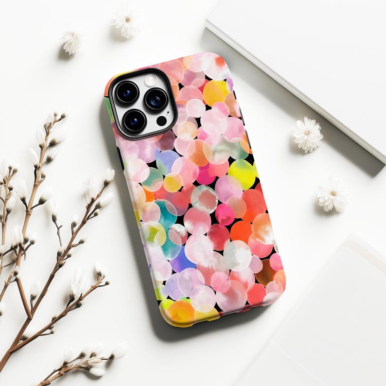 May include: A colorful phone case with a vibrant pattern of overlapping watercolor circles in shades of pink, orange, yellow, and blue against a black background. The case has a black camera lens area and a yellow and green border.