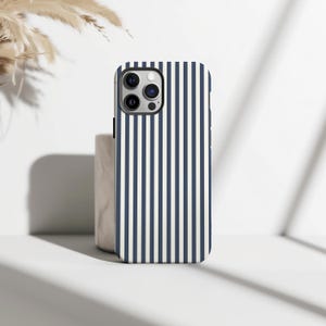 May include: A navy blue and white striped smartphone case. The case features a vertical stripe design and a camera aperture. The case is designed to protect the phone from damage. The case is made of a hard material.