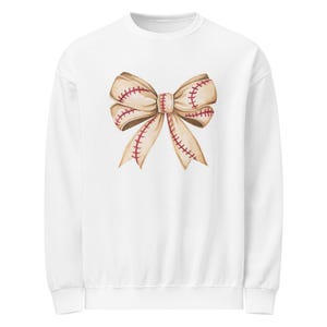 Puede incluir: Sudadera blanca con un gráfico de lazo inspirado en el béisbol. El lazo es de color beige con costuras rojas, que recuerdan a una pelota de béisbol. El diseño está centrado en la parte delantera, ofreciendo un look deportivo y elegante.