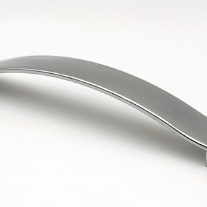 Può includere: Maniglia per mobili argentata lucida con un design curvo. La maniglia presenta una base rettangolare a ciascuna estremità e un centro leggermente arcuato. Adatta per cassetti e armadi. Misura circa 15 cm.
