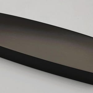 Puede incluir: Objeto rectangular de color marrón oscuro con bordes redondeados. La superficie tiene una textura cepillada y el objeto parece estar hecho de un material sólido. El artículo está sobre un fondo blanco liso.