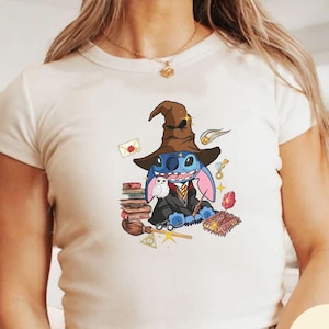 May include: A white crop top featuring a blue Stitch character dressed as a witch, holding a wand and surrounded by books, a broom, and other magical items.