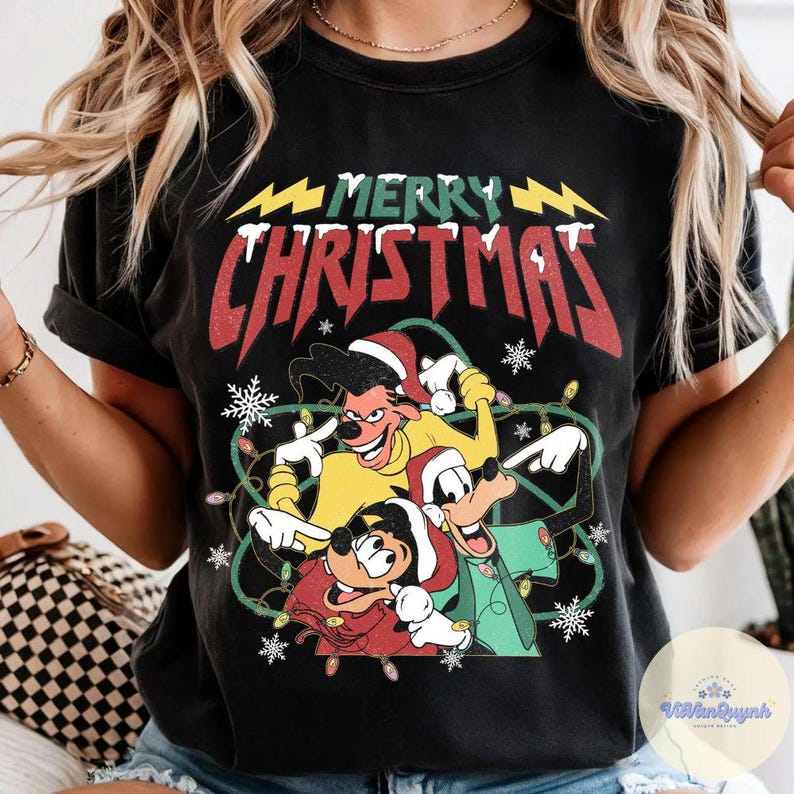 May include: Black t-shirt featuring a graphic of cartoon characters in Santa hats with the text "MERRY CHRISTMAS" in red and white. The design includes snowflakes and string lights, creating a festive holiday theme.