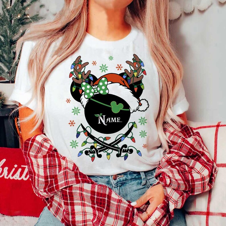 May include: White t-shirt featuring a festive design with a black Mickey Mouse head wearing a Santa hat and reindeer antlers. The design includes a green bow, snowflakes, and string lights. The word "Name" is printed on the design.