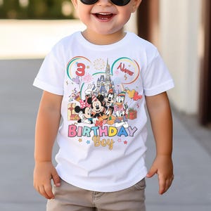 May include: White t-shirt featuring a colorful graphic of Disney characters, including Mickey Mouse, Minnie Mouse, Donald Duck, and Goofy, with a castle and the text "Birthday Boy". The number "3" and the word "Name" are also displayed.